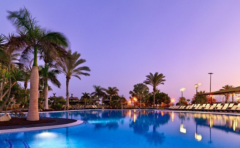 A serene resort pool surrounded by palm trees at dusk, a tranquil setting for Jive Addiction events.