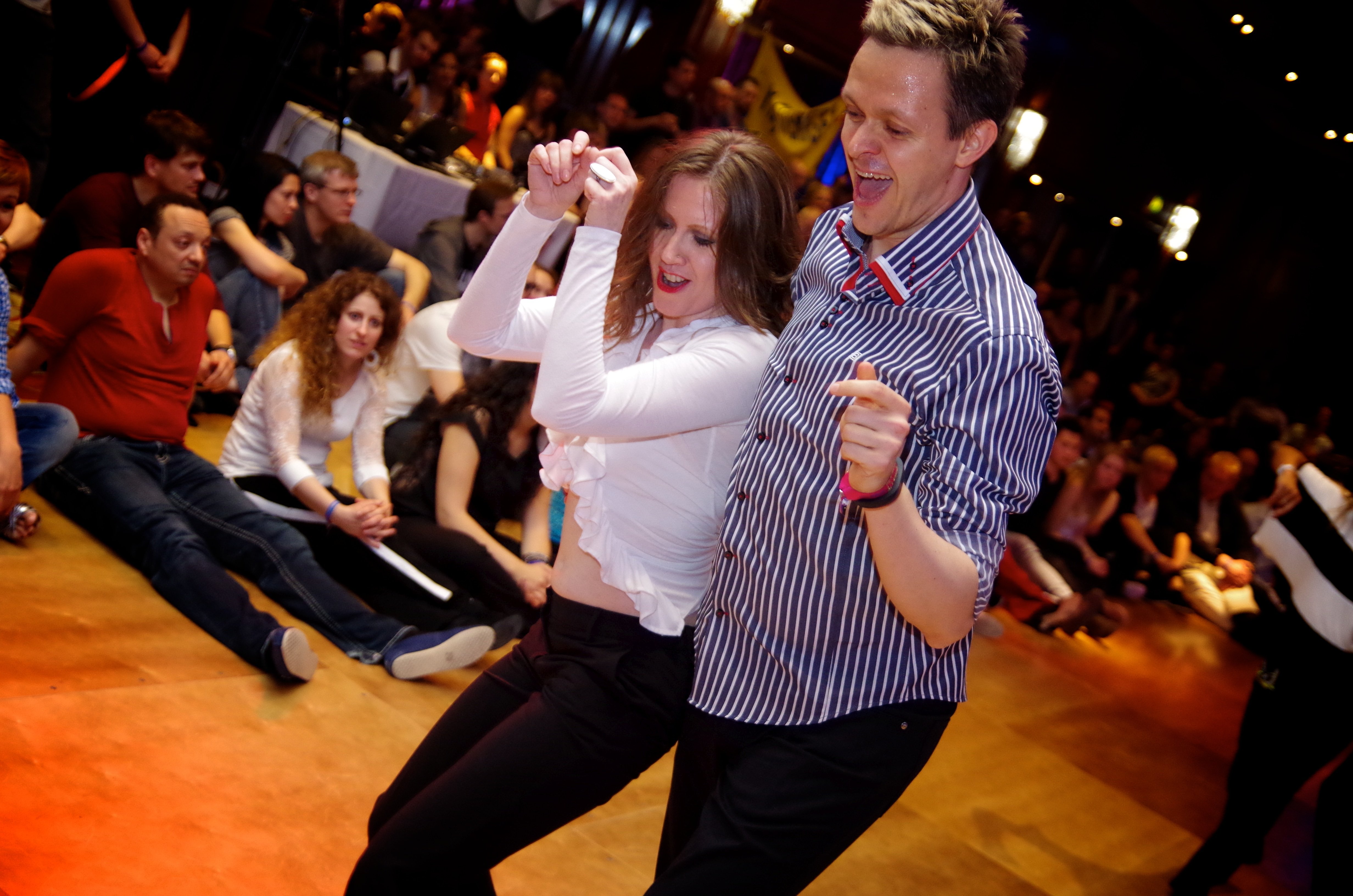 A dancing couple at a Jive Addiction event, joyfully moving to the music with an engaged audience watching.