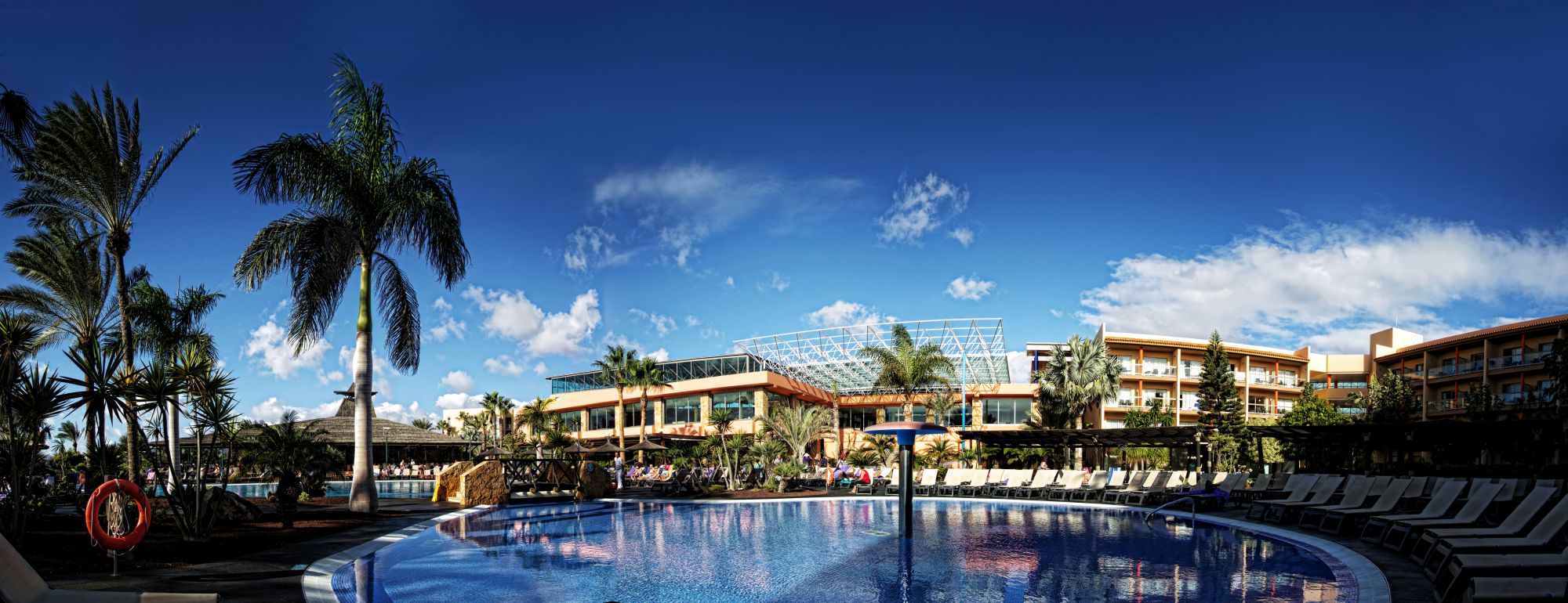 A luxurious resort poolside with palm trees and a clear blue sky, a venue for Jive Addiction dance events.
